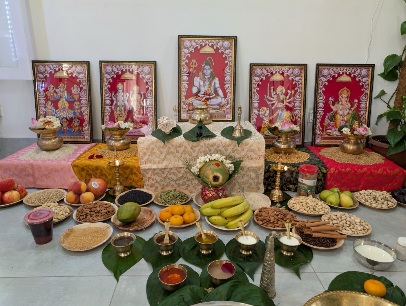 Puja altar with framed deities, brass lamps, fruit and offerings on leaves